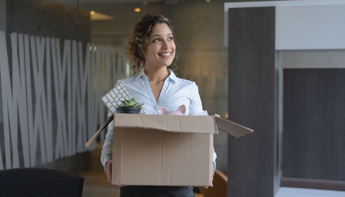 smling young woman holding a box filled with her office supplies after resigning from a job