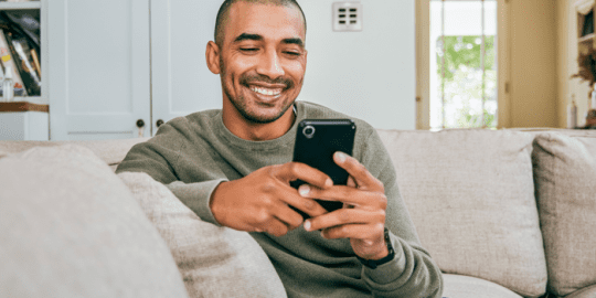 young man sitting on sofa smiling and holding smartphone with both hands