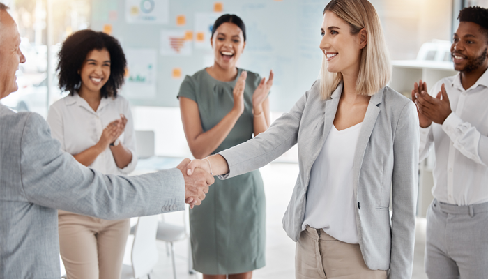 group of people in an office with one man shaking the hand of a woman new hire