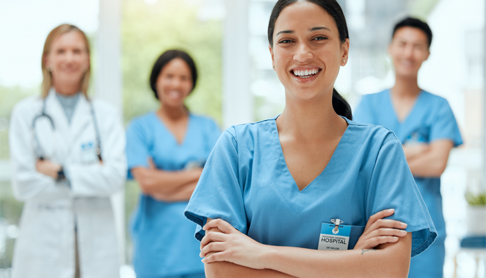3 blurred nurses and doctors in background and one female nurse in focus smiling indicating reference checks in the healthcare industry