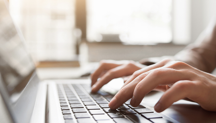 close up of hands typing on laptop indicating completion of a vulnerable sector check