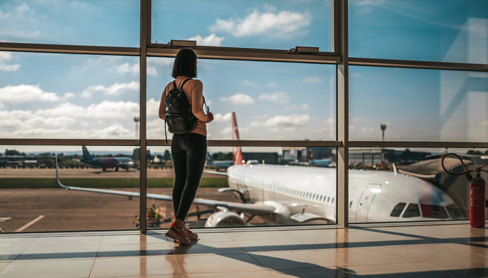 woman at airport looking out the window at airplane on tarmack